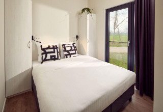 Dormitorio de lodge moderno con cama doble, armarios, cojines decorativos y gran ventanal al exterior.