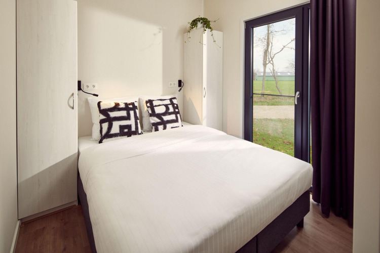 Dormitorio de lodge moderno con cama doble, armarios, cojines decorativos y gran ventanal al exterior.