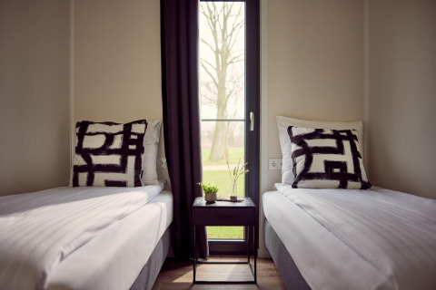 Zwei Einzelbetten mit modernen Kissen und Nachttisch dazwischen in einem gemütlichen Lodge-Zimmer.