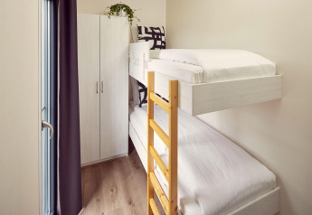 Petite chambre dans un lodge avec lits superposés, échelle en bois, armoire et lumière naturelle de la fenêtre.