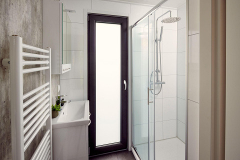 Moderne og kompakt badeværelse på et lodge med bruser, vask, opvarmet håndklædetørrer og glasdør.