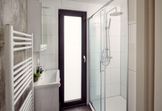 Baño moderno y compacto en un lodge, con ducha, lavabo, toallero calefactable y puerta de cristal.