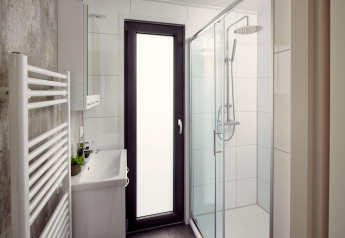 Salle de bain moderne et compacte dans un lodge avec douche, lavabo, porte vitrée et sèche-serviettes.