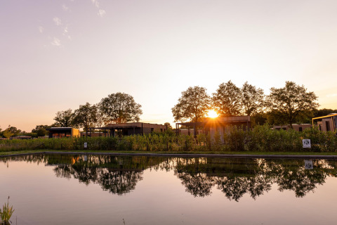 Atardecer en Water lodge 6 Deluxe con sauna y jacuzzi junto a un estanque en Hofparken Wiltershaar, Países Bajos.