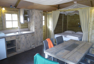 Interior de una acogedora Camphome lodge con cocina, mesa de comedor y cama en Holiday Park Witterzomer.