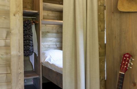 Vista interior de una lodge Camphome en Holiday park Witterzomer, con paredes de madera, cama y guitarra.