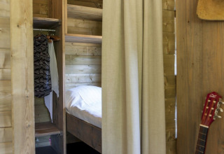 Vista interior de una lodge Camphome en Holiday park Witterzomer, con paredes de madera, cama y guitarra.