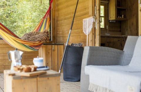 Veranda van lodge met kleurrijke hangmat, stoel en boszicht bij Camphome, Witterzomer, Nederland.