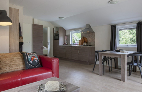 Interior of a chalet at Holiday park Witterzomer with red sofa, dining table and modern kitchen in natural light.
