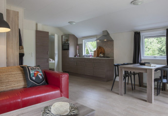Interior de un chalet en Holiday park Witterzomer con sofá rojo, mesa de comedor y cocina moderna iluminada.