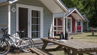 Vista esterna di lodge accoglienti con biciclette e tavolo da picnic in una giornata di sole nella natura.