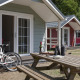 Udendørsbillede af hyggelige lodge-hytter, cykler og picnicbord på en solrig dag i naturen.