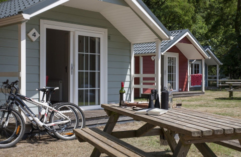 Buitenaanzicht van gezellige lodge-huisjes met fietsen en picknicktafel op een zonnige dag in het groen.