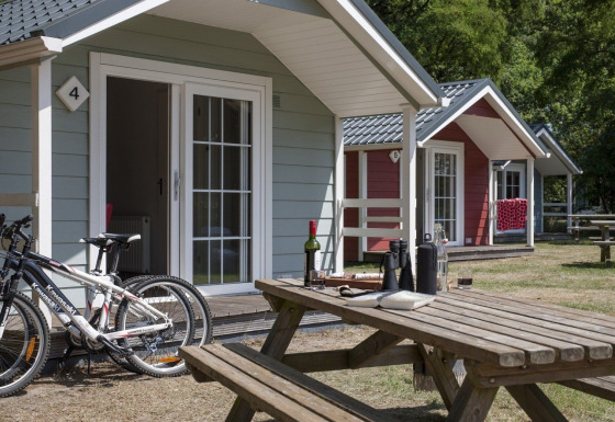 Udendørsbillede af hyggelige lodge-hytter, cykler og picnicbord på en solrig dag i naturen.