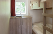 Dormitorio pequeño con literas, armario de madera, ventana y cortina roja en la Lodge de Witterzomer.