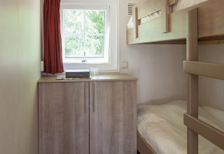 Dormitorio pequeño con literas, armario de madera, ventana y cortina roja en la Lodge de Witterzomer.