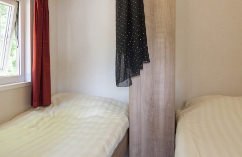 Zwei Einzelbetten in einem kleinen Zimmer mit Fenster und rotem Vorhang in der Lodge im Holiday park Witterzomer.
