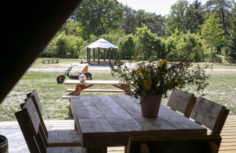 Vue d'une tente safari au Holiday park Witterzomer avec table en bois, fleurs et aire de jeux extérieure.
