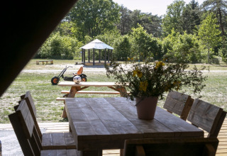 Vue d'une tente safari au Holiday park Witterzomer avec table en bois, fleurs et aire de jeux extérieure.