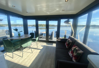 Soggiorno moderno di Houseboat Marina Mookerplas con grandi finestre e vista panoramica sul lago tranquillo.