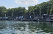 Casa flotante moderna en Marina Mookerplas, Países Bajos, rodeada de árboles y reflejada en el agua.