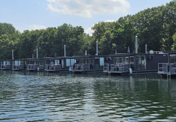 Moderni houseboat ormeggiati a Marina Mookerplas, Paesi Bassi, circondati da alberi e acqua calma.