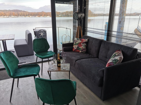 Gemütlicher Wohnraum auf dem Hausboot Marina Mookerplas mit Seeblick, grünen Stühlen und Sofa.