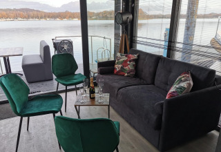 Indbydende stue på Houseboat Marina Mookerplas med udsigt til søen, grønne stole og sofa.