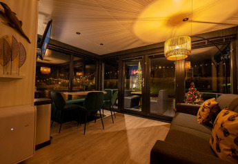 Accogliente soggiorno nella Houseboat Marina Mookerplas con decorazioni natalizie e vista sul lago notturno.