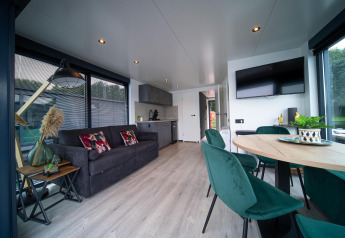 Moderne stue på Houseboat Marina Mookerplas med sofa, spisebord, grønne stole og stort vindue.