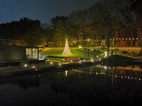 Foto nocturna de Houseboat Marina Mookerplas con luces navideñas, árbol y reflejos en el agua.