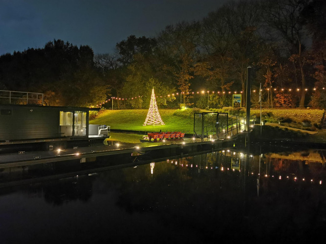 Foto nocturna de Houseboat Marina Mookerplas con luces navideñas, árbol y reflejos en el agua.