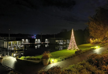 Nattestemning ved Houseboat Marina Mookerplas i Holland, med oplyst juletræ ved vandet og husbåde.