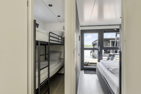 Interior de una casa flotante con una habitación de literas a la izquierda y una de cama doble a la derecha.
