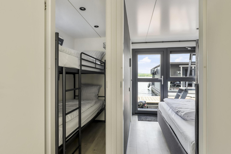 Interior de una casa flotante con una habitación de literas a la izquierda y una de cama doble a la derecha.