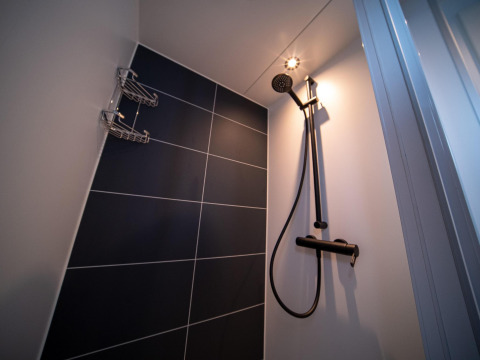 Ducha moderna en una casa flotante, con azulejos oscuros, cabezal de ducha y luz de techo brillante.