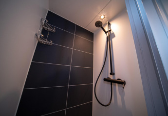 Moderne Dusche mit dunklen Fliesen, Duschkopf und Ablagekörben auf einem Hausboot unter Spotlicht.