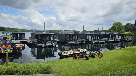 Péniches modernes à Houseboat Marina Mookerplas avec vélos électriques et petit bateau sous ciel nuageux.