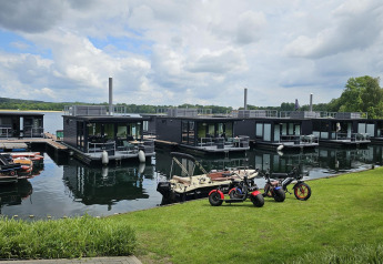 Péniches modernes à Houseboat Marina Mookerplas avec vélos électriques et petit bateau sous ciel nuageux.