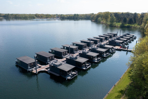 Vista aérea de modernas casas flotantes en la Marina Mookerplas, rodeadas de agua y vegetación.