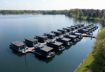 Vista aerea di moderne case galleggianti alla Houseboat Marina Mookerplas circondate da acqua e alberi.