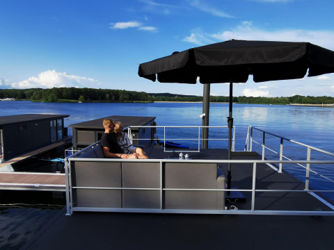 Ein Paar sitzt unter einem schwarzen Sonnenschirm auf einem Hausboot bei Marina Mookerplas, Niederlande.