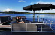 Een stel zit onder een zwart zonnescherm op het terras van een woonboot bij Marina Mookerplas in Nederland.