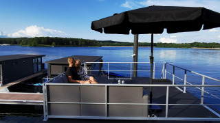 Ein Paar sitzt unter einem schwarzen Sonnenschirm auf einem Hausboot bei Marina Mookerplas, Niederlande.
