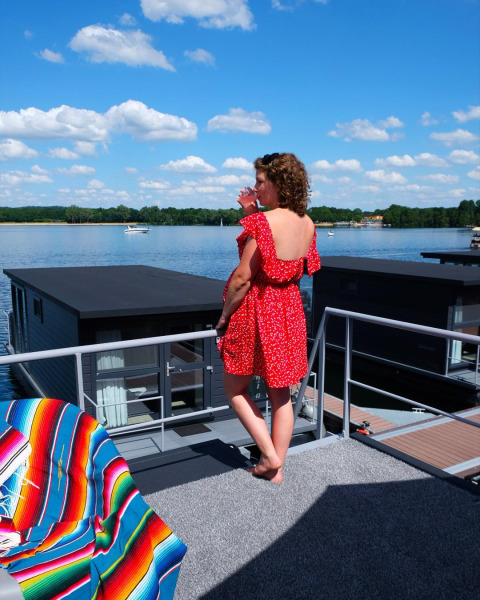 Mujer con vestido rojo en una casa flotante en Marina Mookerplas, Países Bajos, junto al lago soleado.