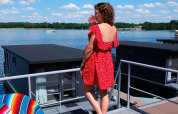 Mujer con vestido rojo en una casa flotante en Marina Mookerplas, Países Bajos, junto al lago soleado.
