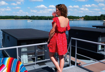 Donna con abito rosso sul houseboat a Marina Mookerplas, Paesi Bassi, vista sul lago e cielo azzurro.