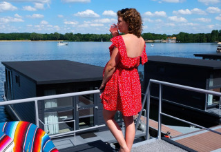 Mujer con vestido rojo en una casa flotante en Marina Mookerplas, Países Bajos, junto al lago soleado.