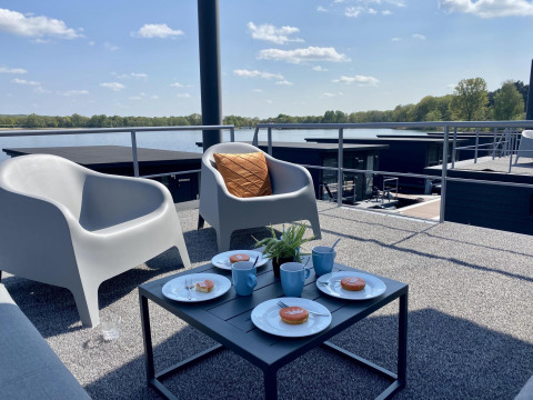 Vista desde Houseboat Marina Mookerplas con asientos exteriores, tazas de café y paisaje junto al lago.