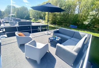 Terrazza sul tetto di Houseboat Marina Mookerplas con divani da esterno, ombrellone e vista sull’acqua.